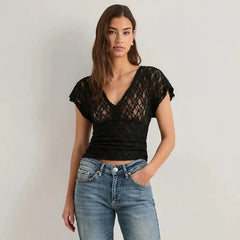 Woman wearing a black lace top and blue jeans against a plain background