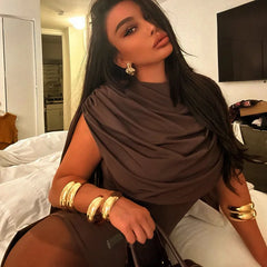 Woman wearing a brown draped top and gold bracelets in a room.