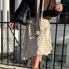 Person wearing a polka dot skirt and brown jacket standing on a balcony.