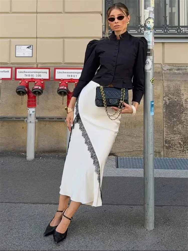 Woman in black top and white skirt standing next to a building with red fire hydrants.