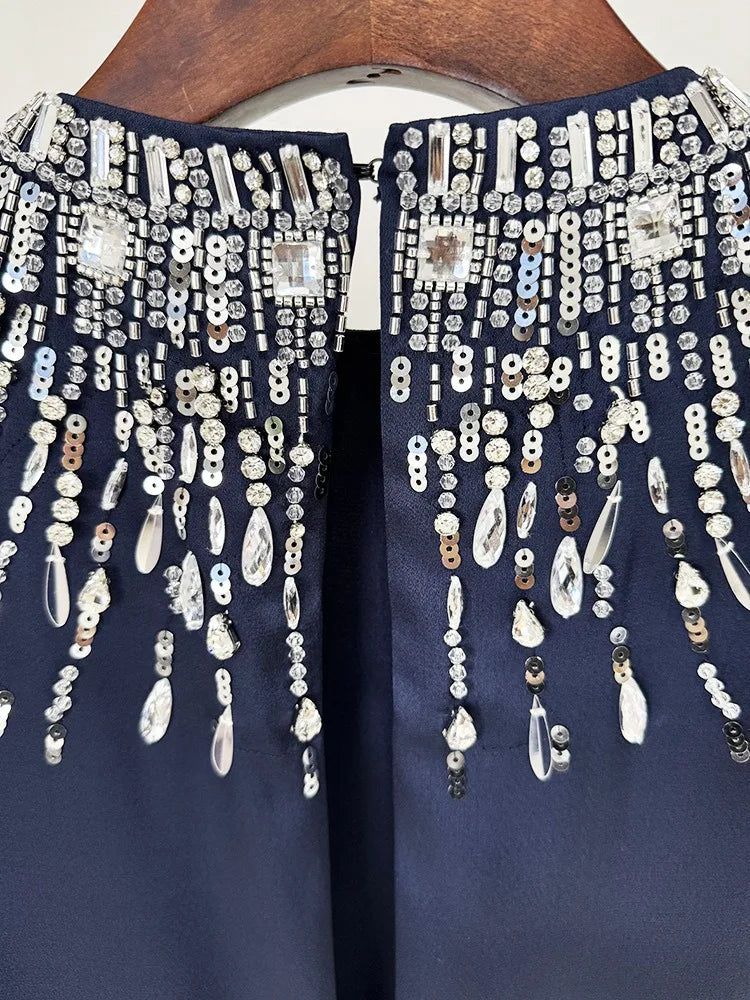 Navy blue garment with intricate silver beadwork on a wooden hanger.