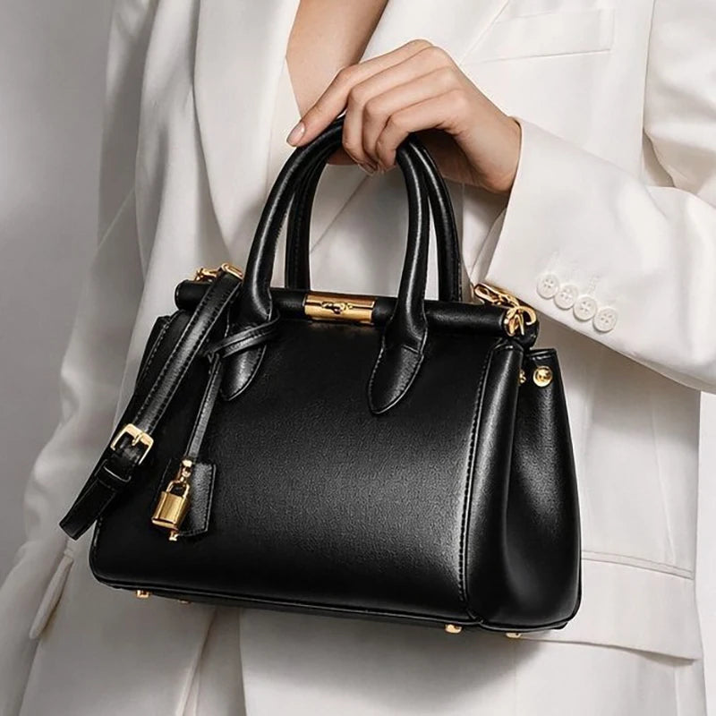 Close-up of a black structured top-handle satchel bag with gold clasp and lock detail.