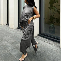 Woman wearing a gray dress walking on a sidewalk with a building and plant in the background.