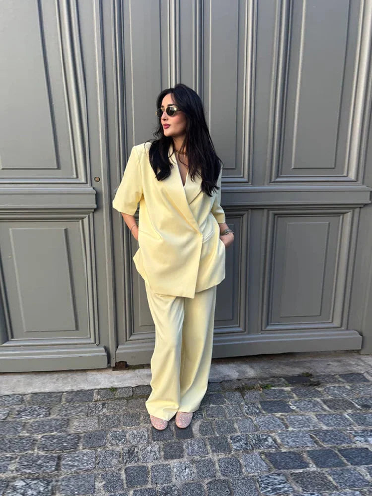 Woman in a light yellow outfit standing in front of a gray door.