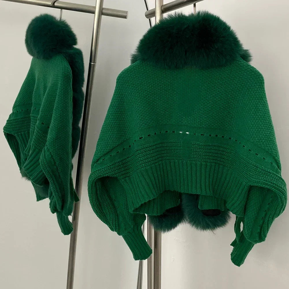Green poncho with fur pom-poms on a stand against a white background