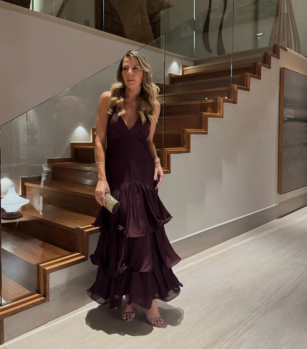 Woman in a dark purple dress standing in a modern interior setting with wooden stairs.