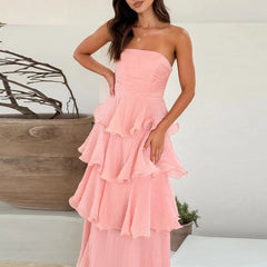 Woman wearing a pink strapless dress with ruffled layers in a minimal indoor setting.