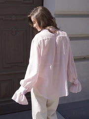 Person wearing a light pink blouse and white pants standing in front of a building entrance.