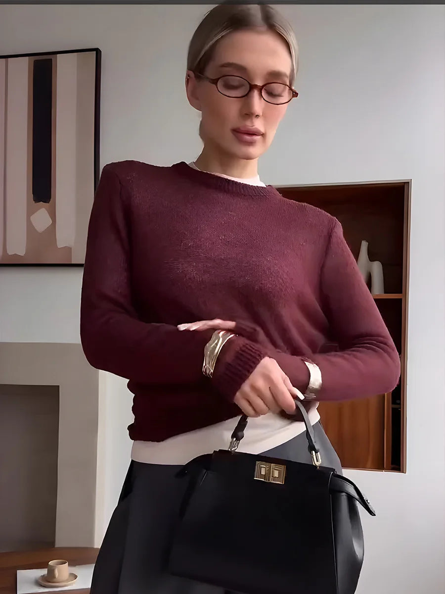 Woman wearing a burgundy sweater holding a black handbag indoors.