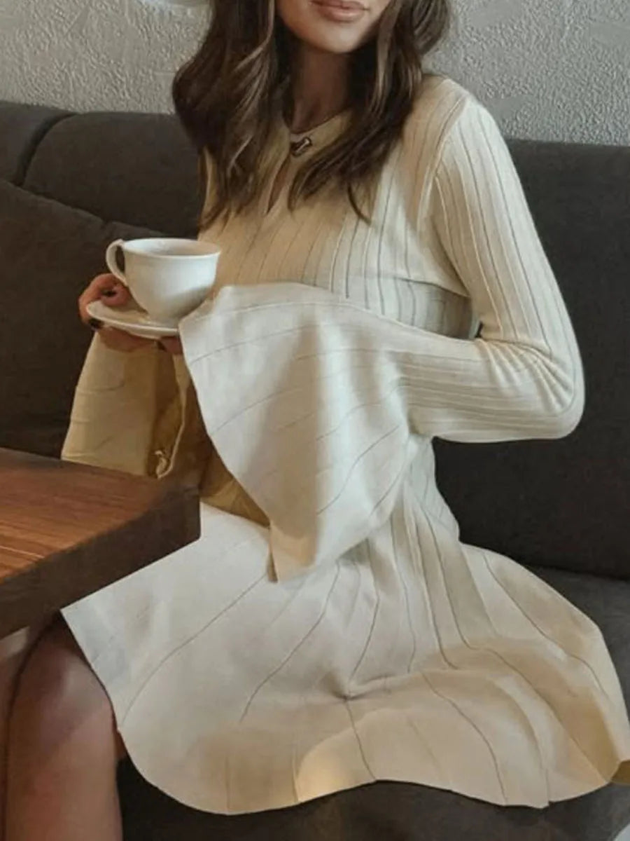 Woman in a beige dress holding a white cup, sitting on a couch.