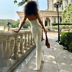 Person in a white jumpsuit holding a red handbag on a stone pathway with greenery and architecture in the background.