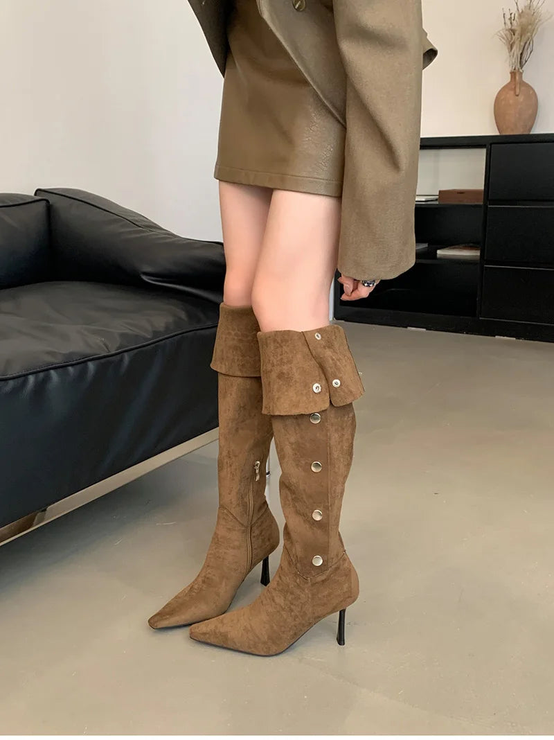 Brown knee-high boots with button details worn by a person in a room.