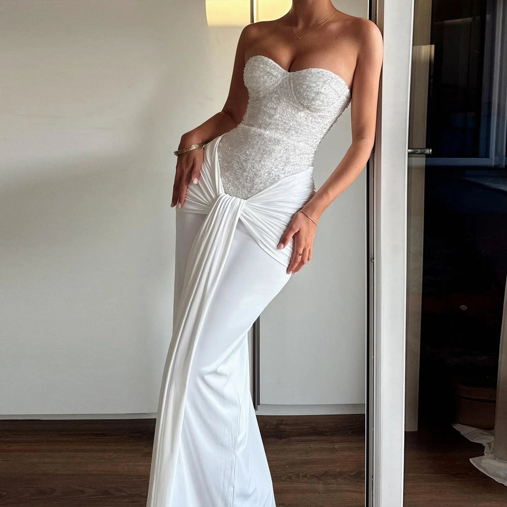 Woman wearing a strapless white gown with a draped skirt in a room.