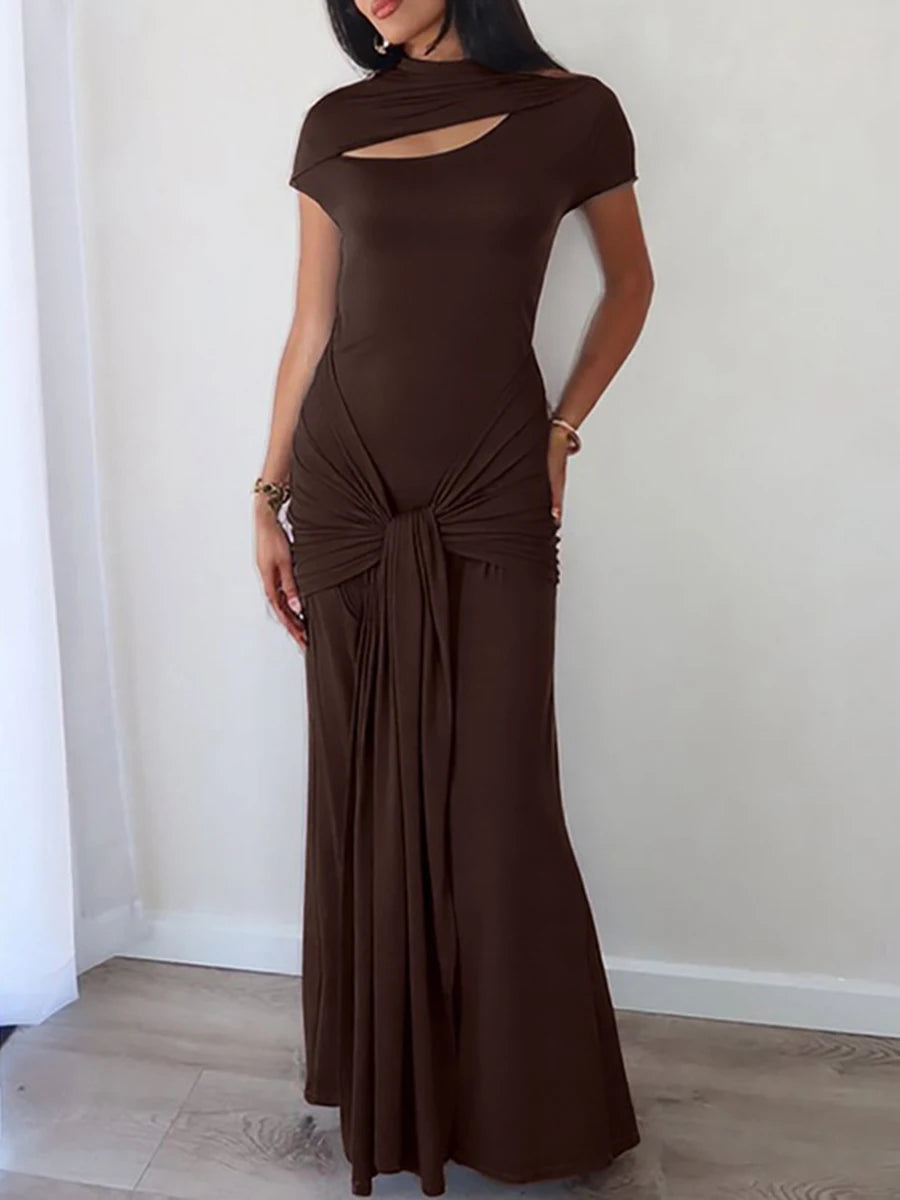 Woman wearing a brown evening gown with a cut-out design against a white wall.
