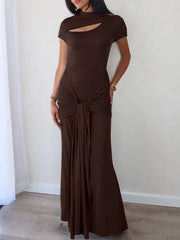 Woman wearing a brown evening gown with a cut-out design against a white wall.