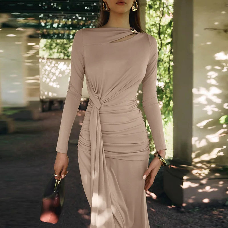 Woman wearing a beige long-sleeve dress with a knot detail, standing outdoors.
