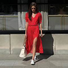 Woman in a red dress with white polka dots standing against a reflective wall.