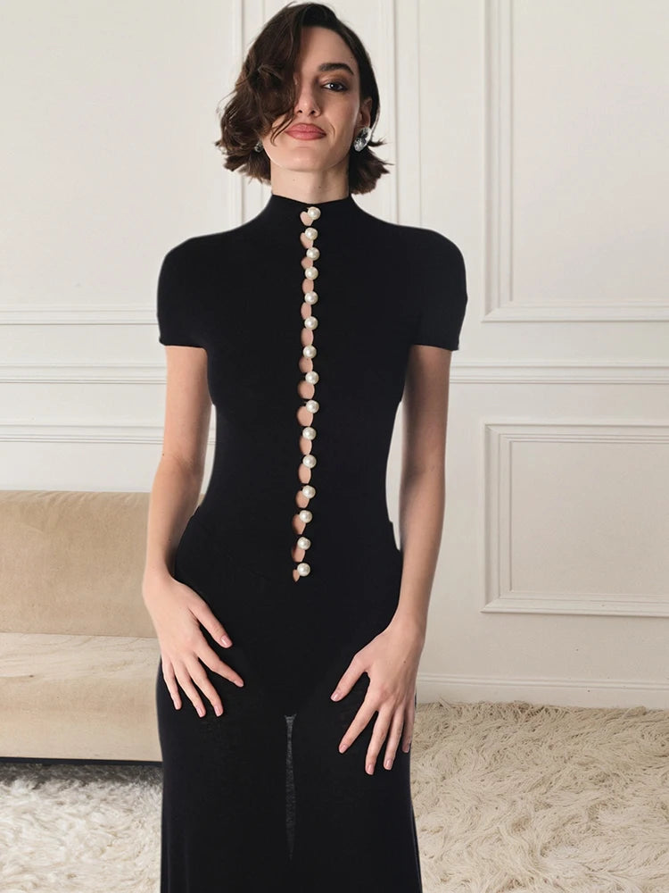 Woman wearing a black outfit with decorative buttons in a room with white walls and a beige carpet.