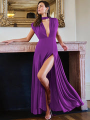 Woman in a purple evening gown with a high slit standing in a room with a mirror and fireplace.