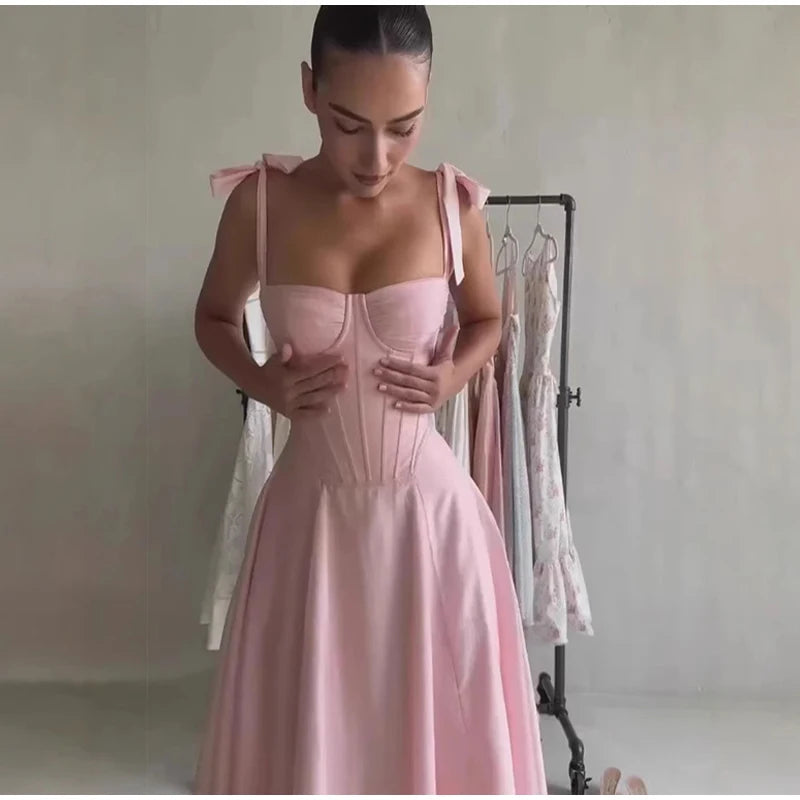 Woman wearing a pink dress with bow straps in a minimalistic setting.