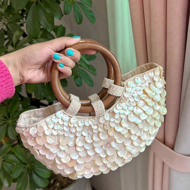 Hand holding a beaded handbag with wooden handles against a blurred indoor background