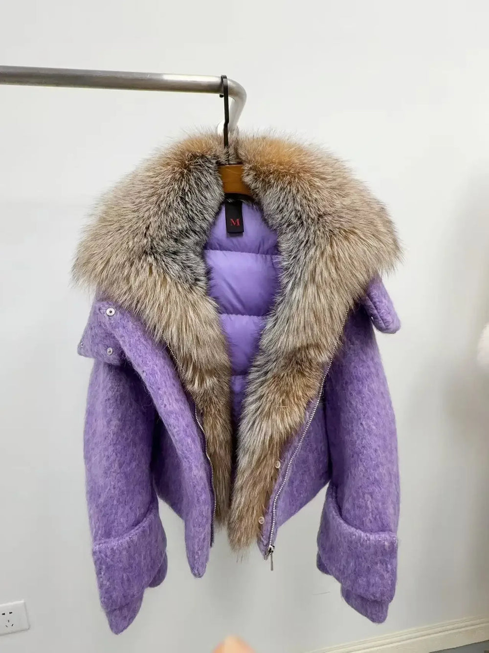 Purple coat with a fur collar hanging on a rack against a white wall.