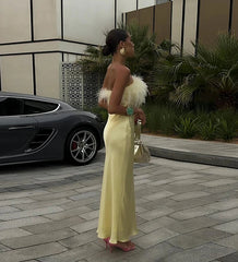 Woman in a yellow dress standing next to a car with a modern building and plants in the background