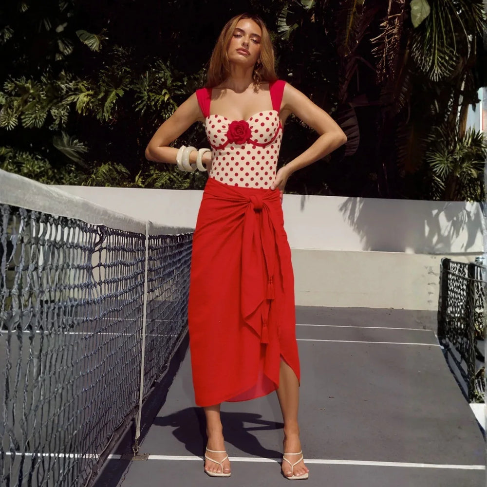 Model wearing polka dot one-piece swimwear with red wrap skirt