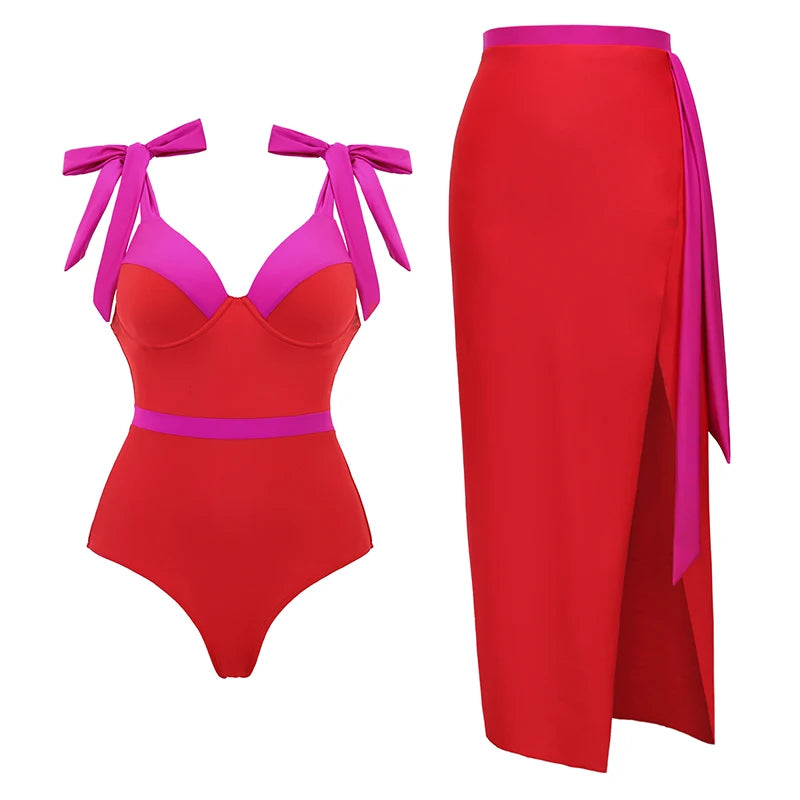 Red and pink contrast trim one-shoulder swimsuit with bow shoulder straps and high-slit red skirt with pink sash.