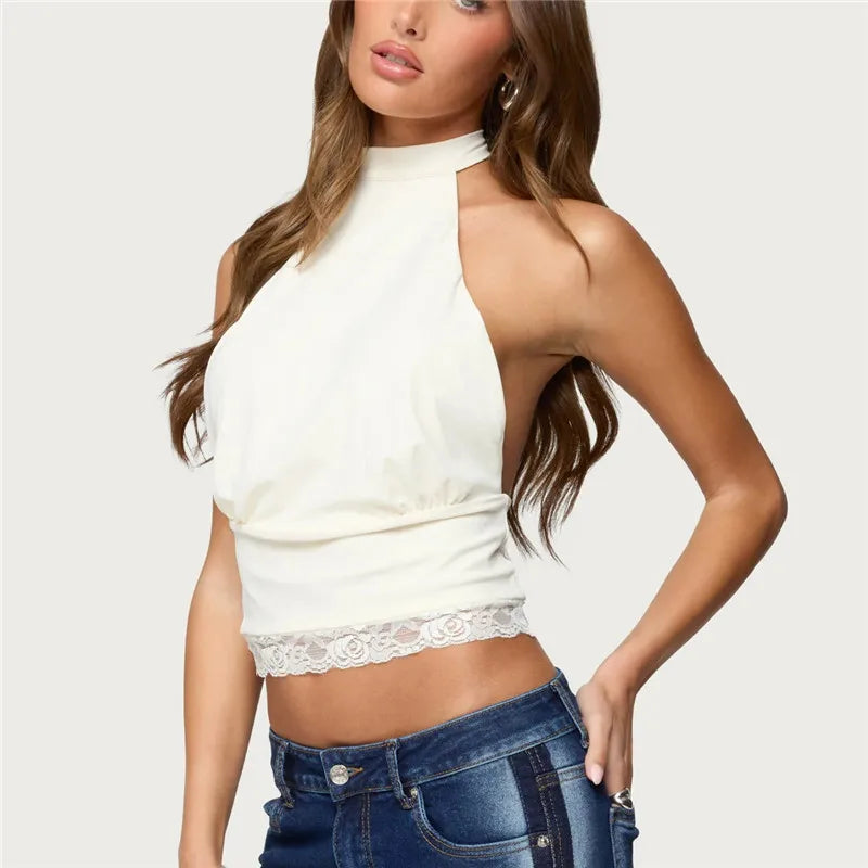 Woman wearing a white halter top with lace details and blue jeans on a light gray background