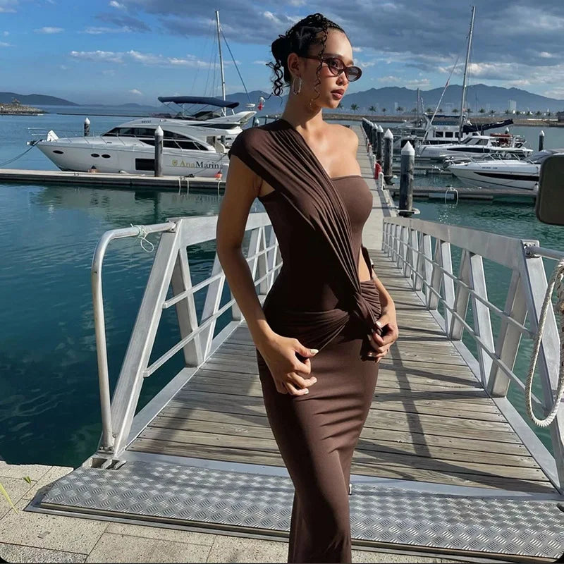 Woman in a brown dress standing on a dock with boats in the background