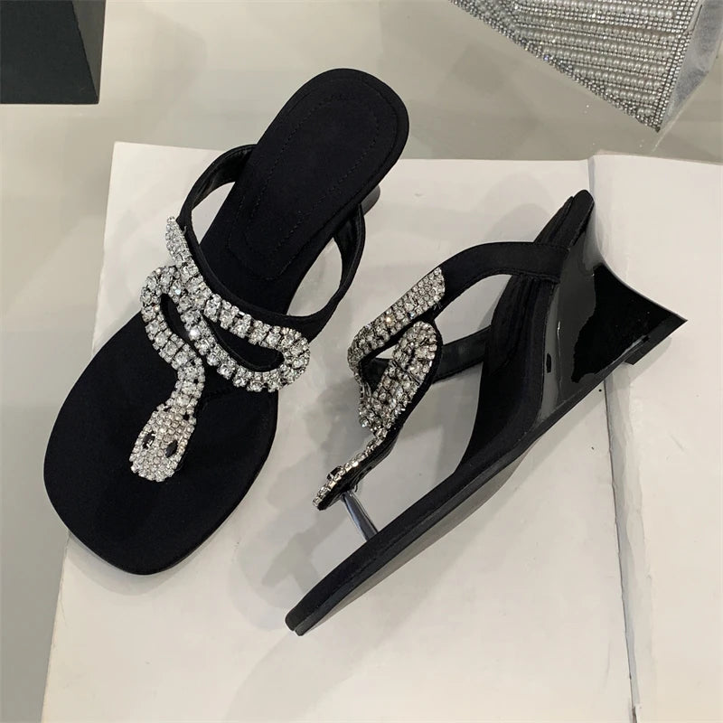 Black high-heeled shoes with rhinestone embellishments on a light gray surface.