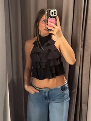 Person wearing a black ruffled top and blue jeans taking a mirror selfie.