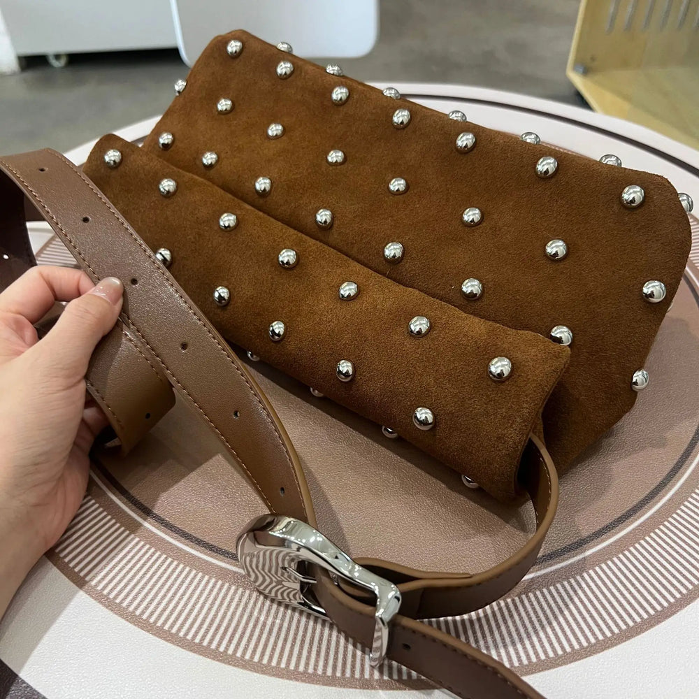 Brown studded handbag with a hand holding it on a round surface.