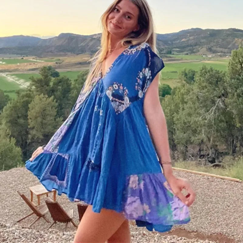 Woman in a blue dress with floral patterns standing outdoors with mountains in the background