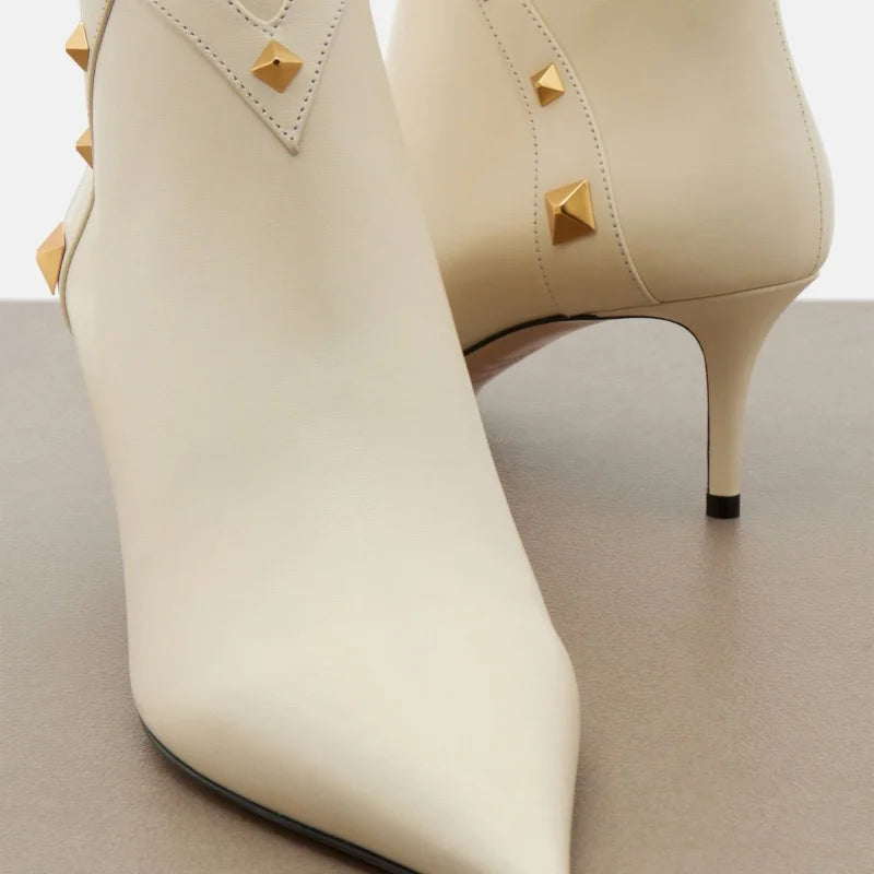 Close-up of white leather pointed toe ankle boots with gold studs, front view.
