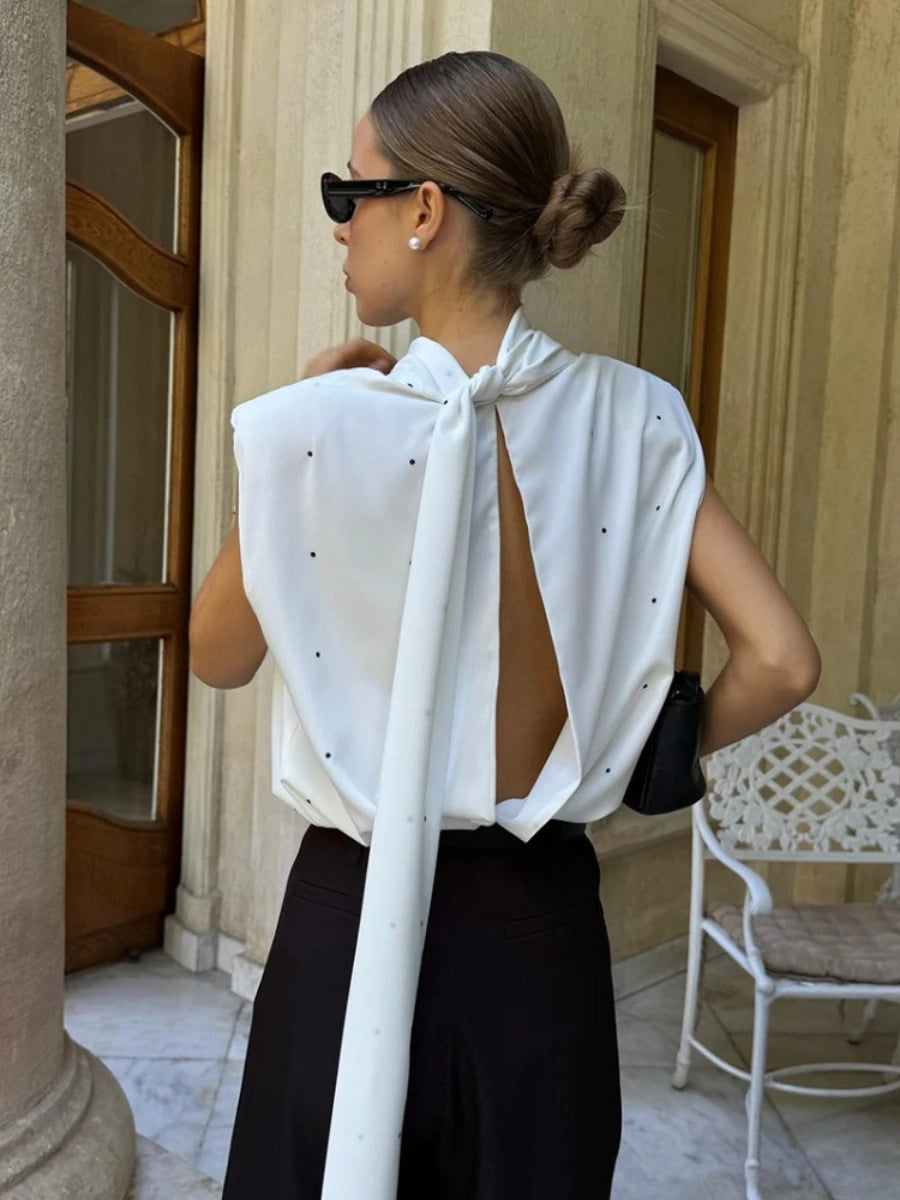 Woman wearing a white blouse with a tie detail and black pants in an outdoor setting.