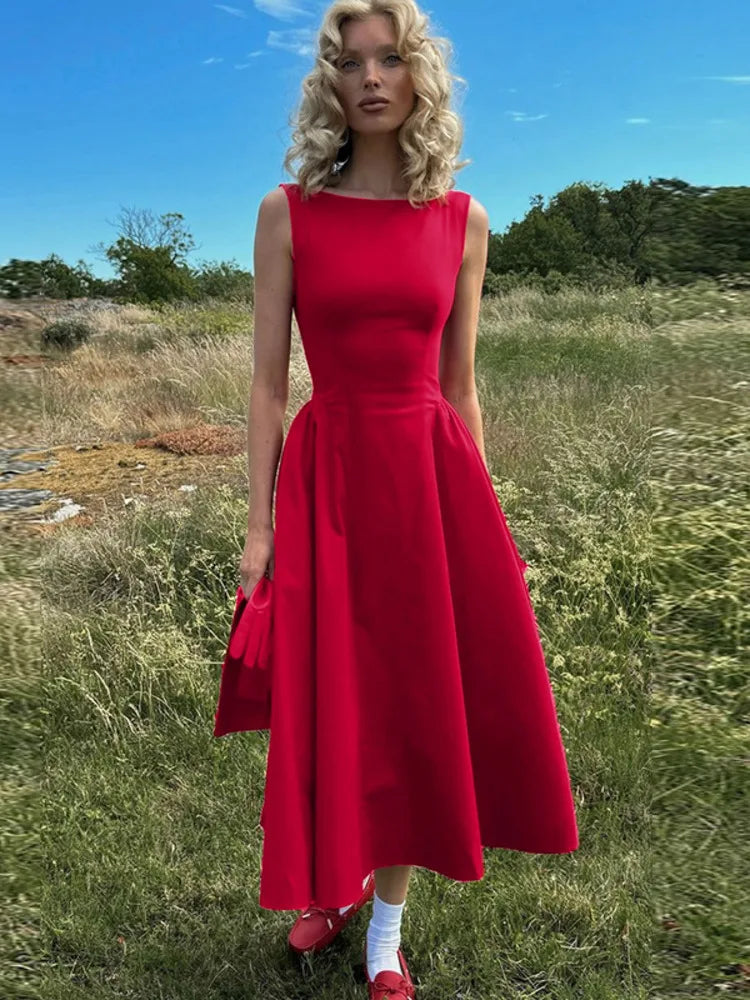 A woman wearing a Red sleeveless A-line midi dress, showcasing the straight neckline and flared skirt.1