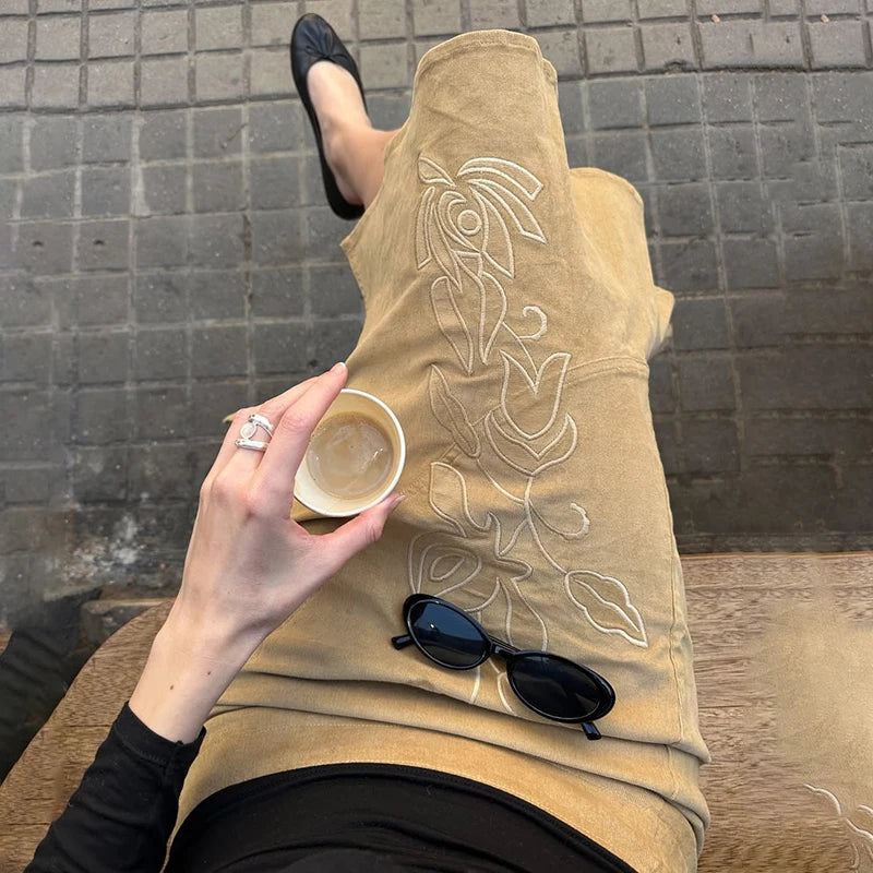 Person holding a cup with a tattooed beige sleeve and sunglasses on a wooden surface.