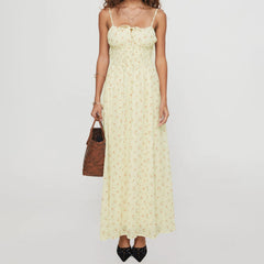 Woman wearing a light yellow floral dress holding a brown handbag on a white background