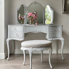 Vintage-style vanity table with three mirrors and a stool in a room.