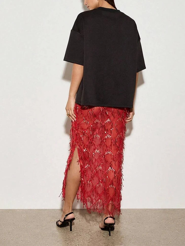 Person wearing a black top and red skirt with floral embroidery on a plain background