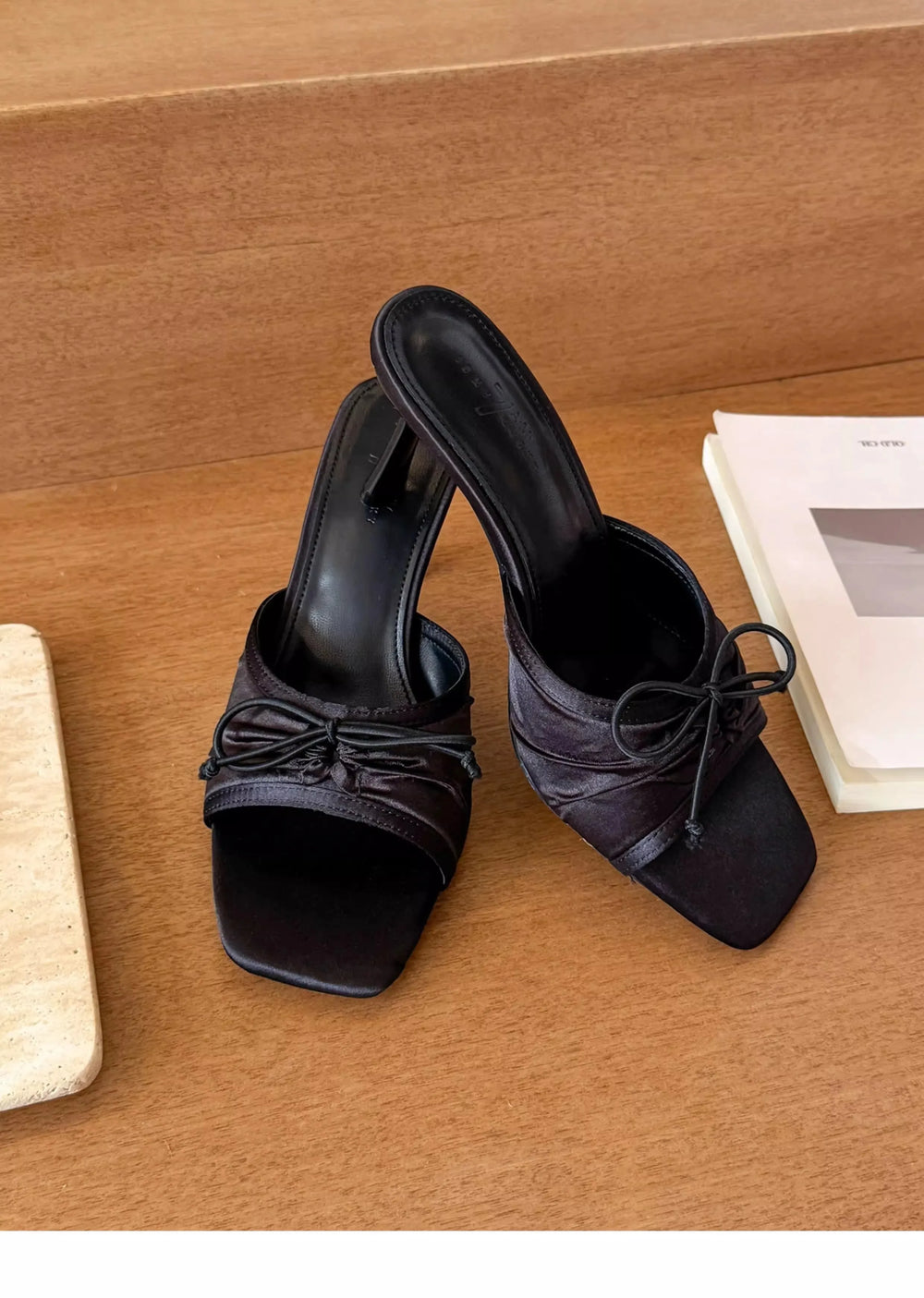 Black high-heeled sandals with bow details on a wooden surface