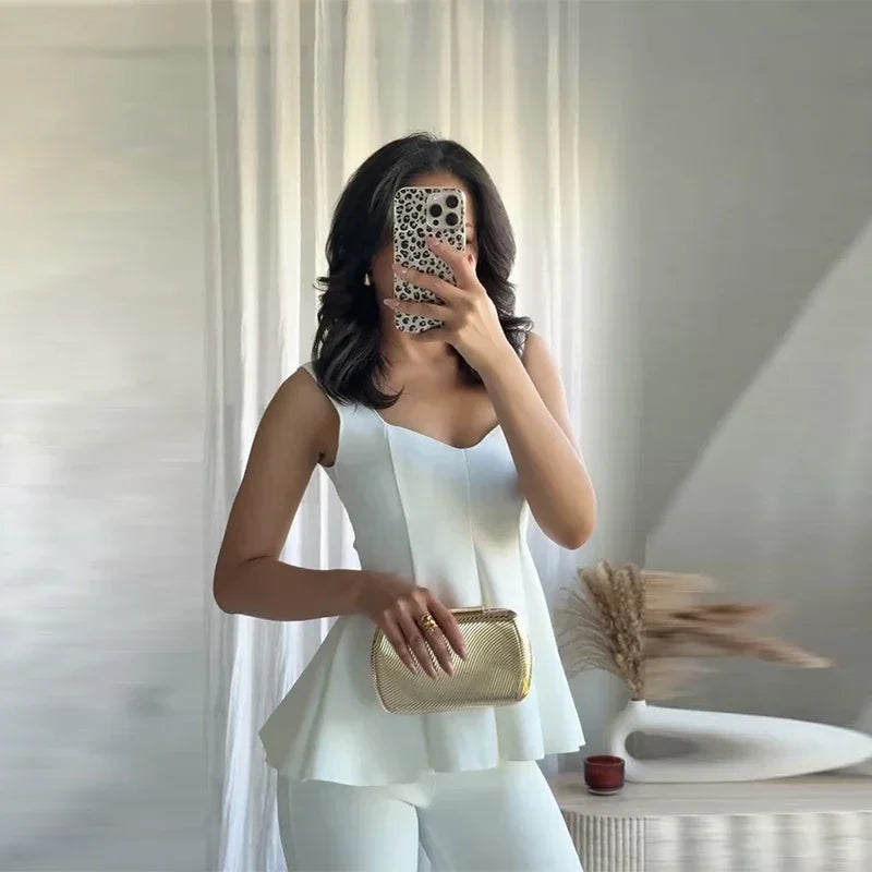 Woman taking a mirror selfie wearing a white sleeveless top and holding a gold clutch.