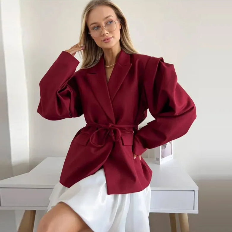 Woman wearing a burgundy blazer over a white dress in a minimalistic setting