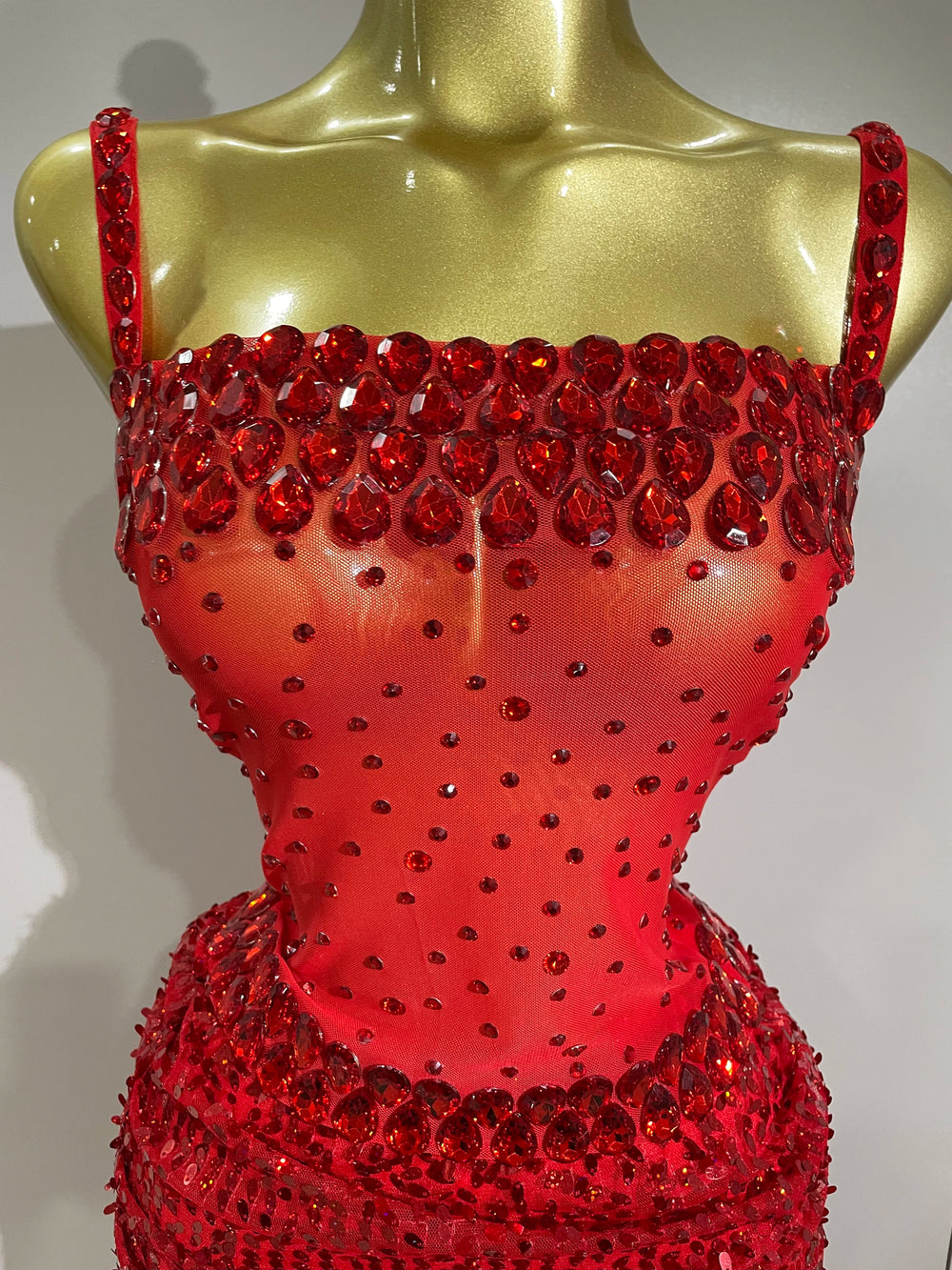 Red beaded top on a gold mannequin against a gray background