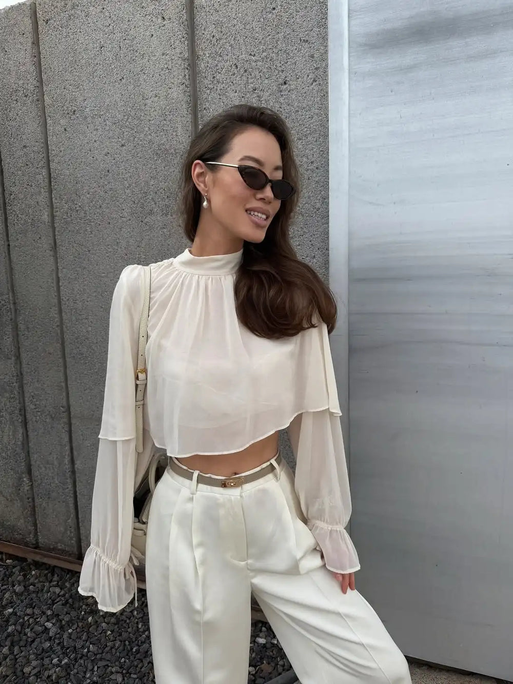 Woman wearing a white outfit with sunglasses against a gray wall.