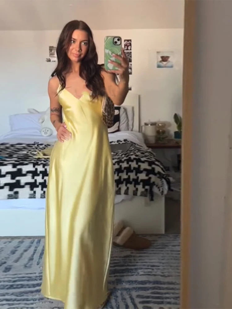 Woman in a yellow satin dress taking a mirror selfie in a bedroom.