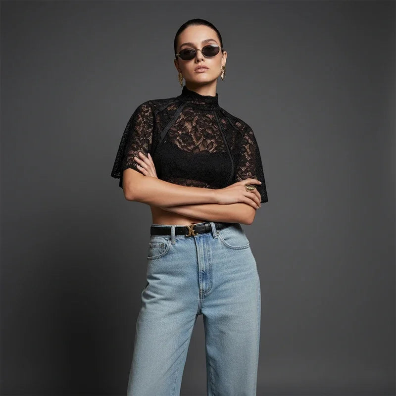 Woman wearing a black lace top and blue jeans against a gray background