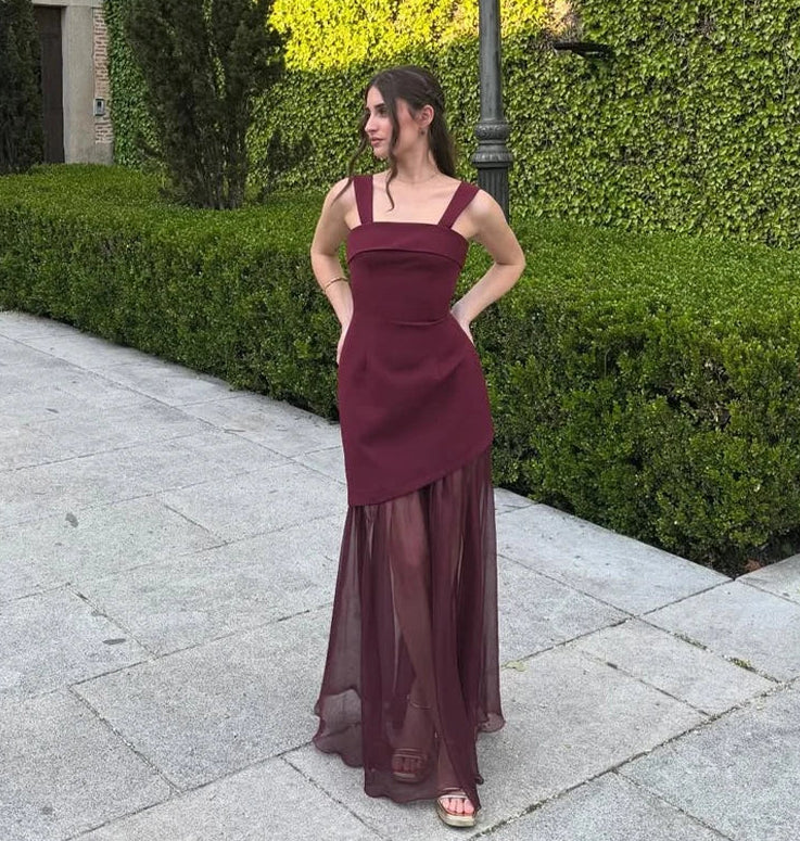 Woman in a burgundy dress standing on a sidewalk with greenery in the background